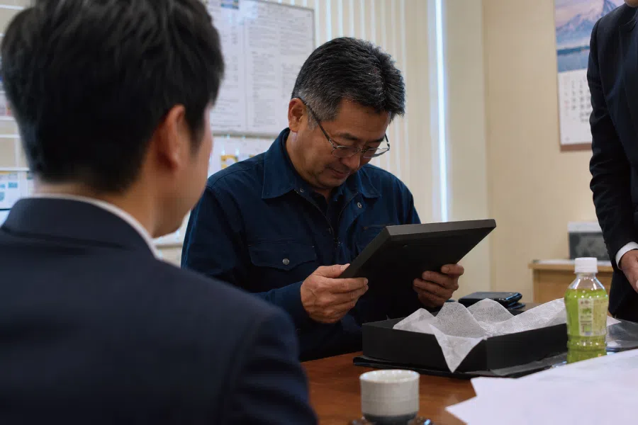 退職祝いの記念品を手に取り見つめる場面
