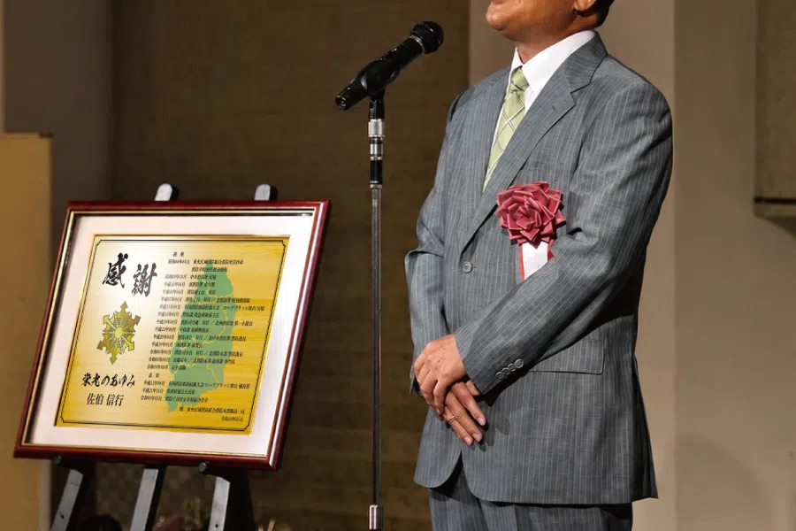 消防士が贈られた記念品を前に挨拶する場面