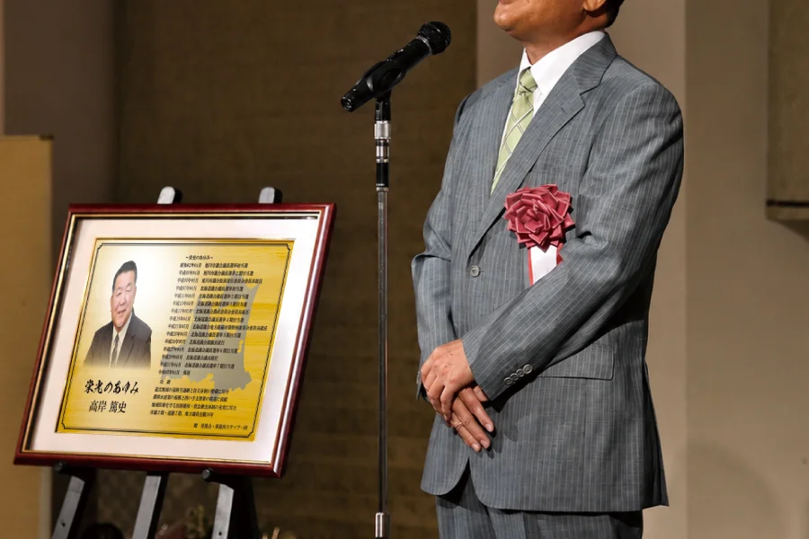 政治家が贈られた勇退祝い・勇退記念品を前に挨拶する場面