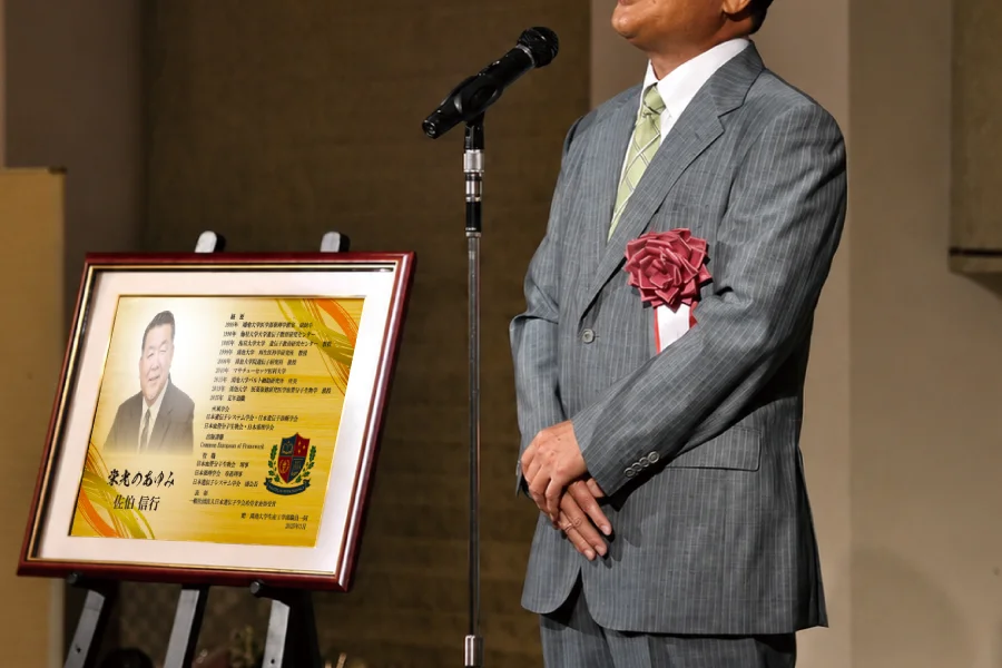 退官する大学教授が教え子から退官記念品を受け取る場面
